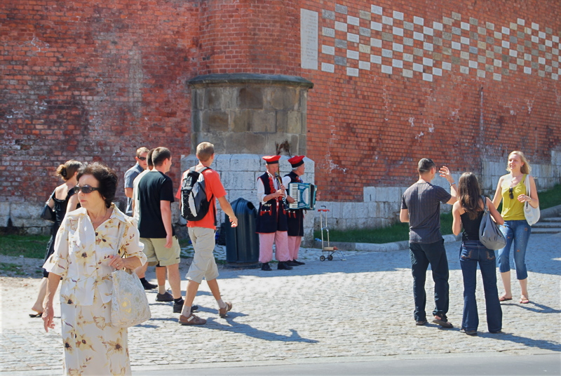 2 - Pedestrians and musicians in traditional regional attire near the defensive brick walls of the Wawel Royal Castle in Kraków, Poland